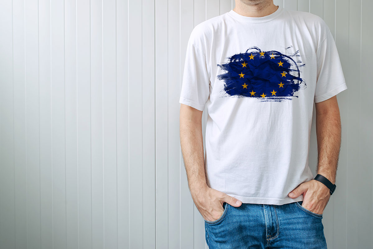 En man har på sig en vit t-shirt med en EU-symbol tryckt på bröstet. Symbolen har en blå bakgrund som ser ut att vara målad med pensel och ovanpå finns de gula stjärnorna.