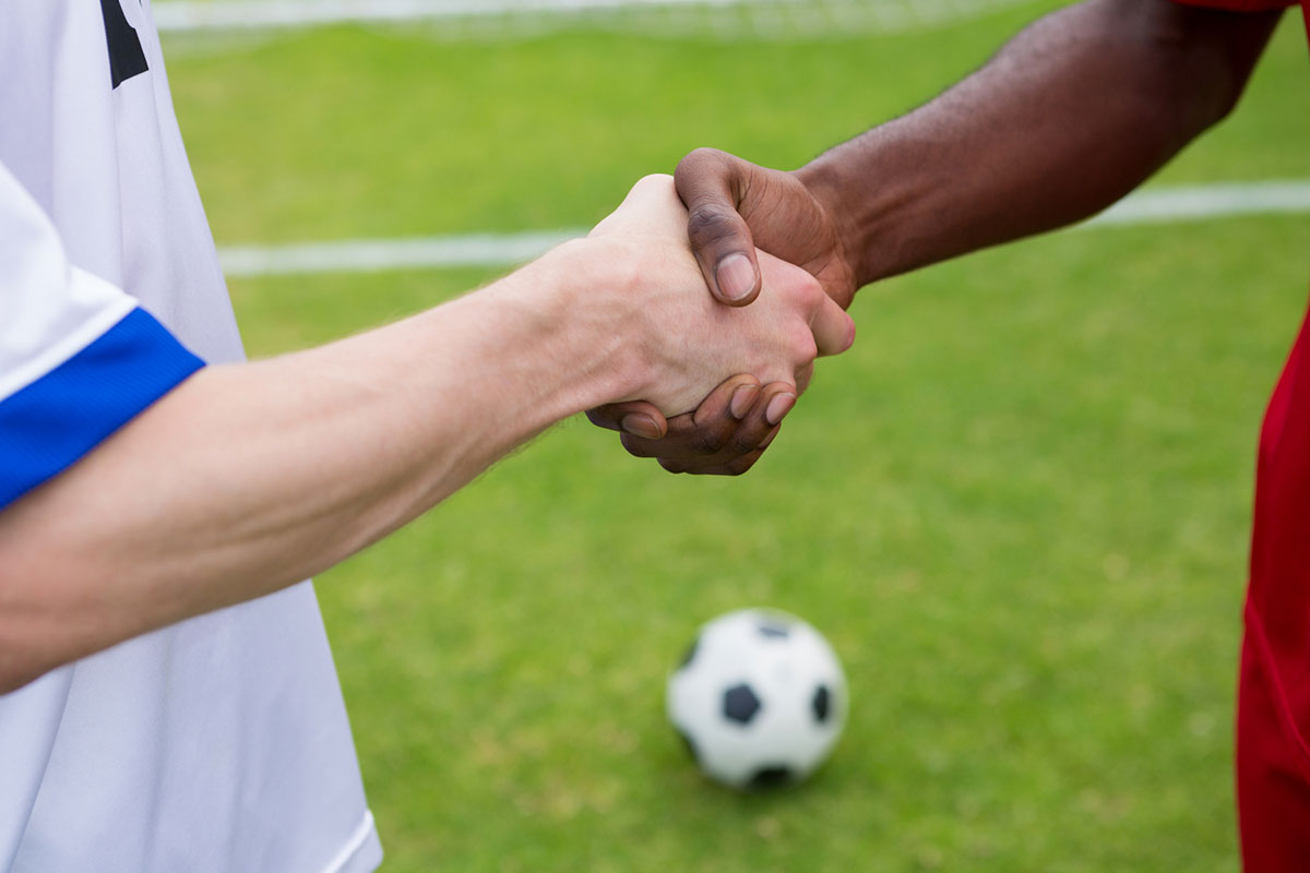 En mörkhyad och en ljushyad fotbollsspelare tar i hand.