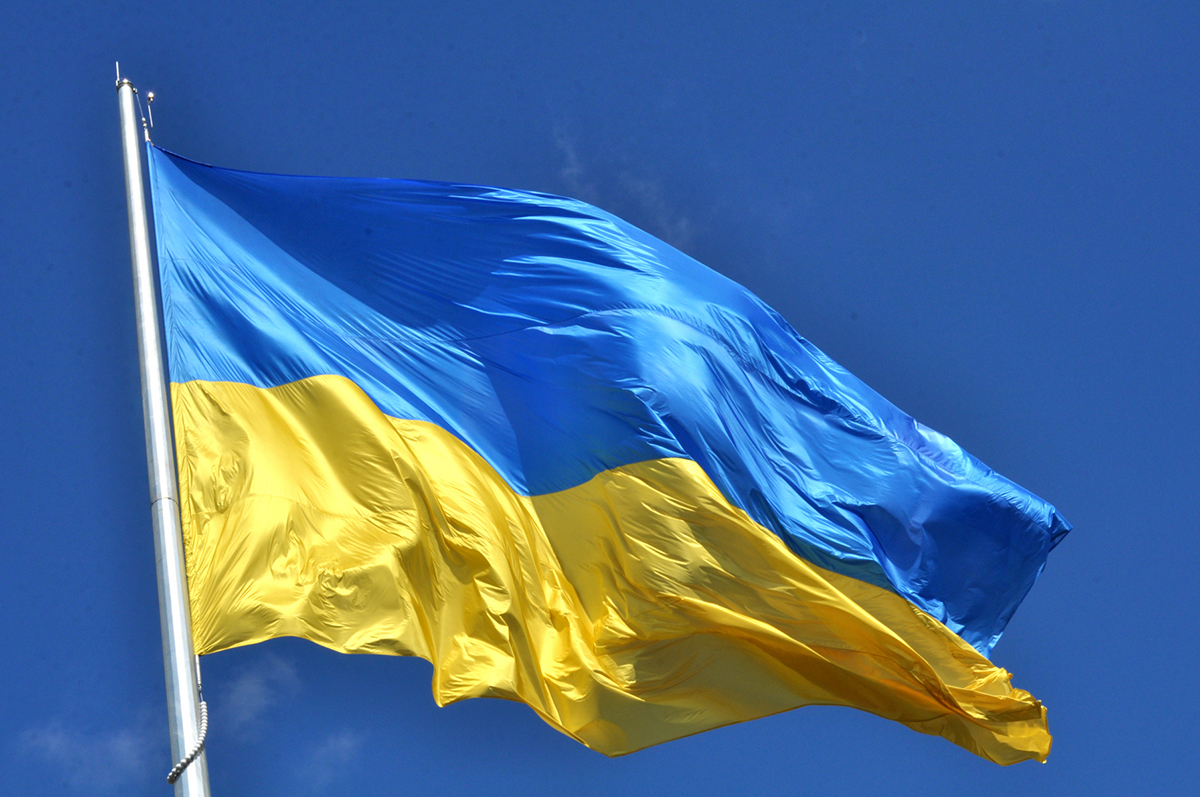 Ukrainas blå-gula flagga vajar i vinden mot en blå himmel.