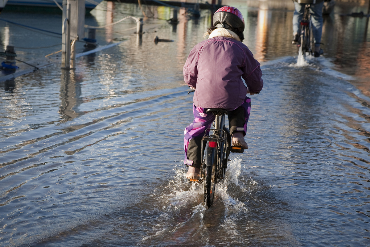 Barn cyklar på översvämmad gata